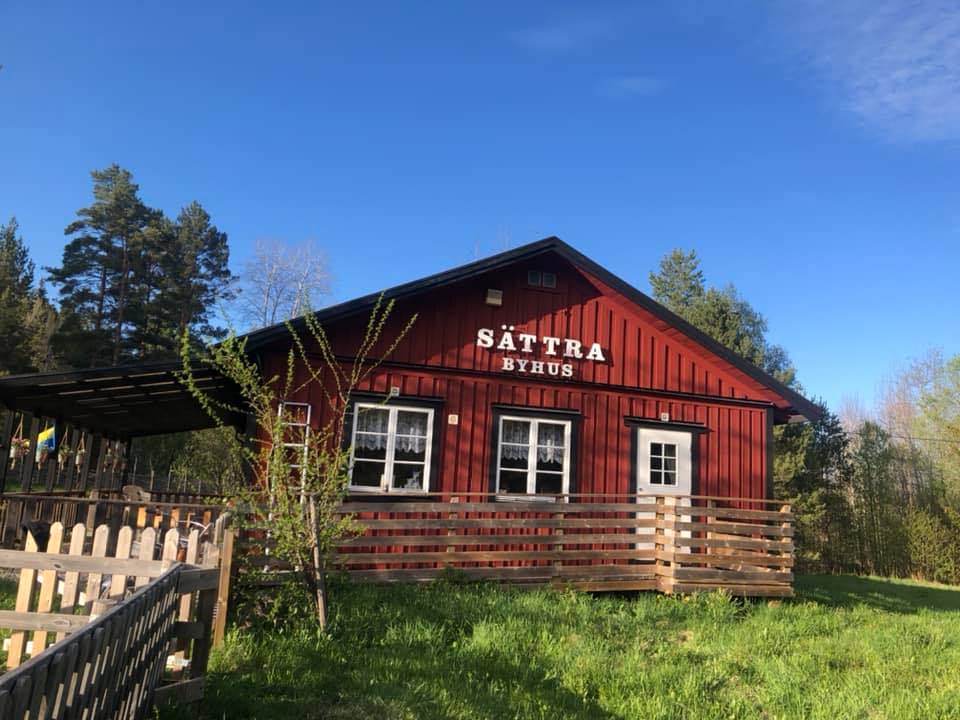 Sättra Byhus, en röd bygdegård omgiven av grönska